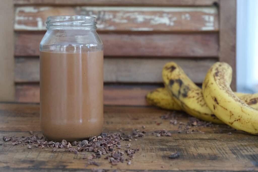 choc butter smoothie in a jar with bananas behind