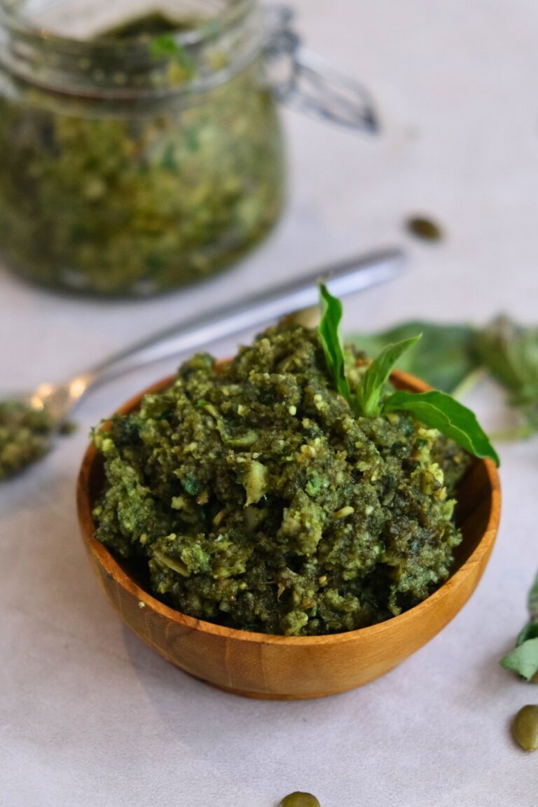 Pepita pesto in a small wooden bowl with a gar full of pesto behind