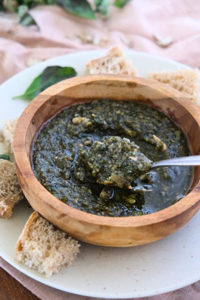 vegan nut free pesto made with sunflower seeds in a wooden bowl with spoon and bread on the side