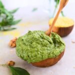 picture of walnut pesto in a wooden small bowl with walnuts, basil and nutritional yeast around it