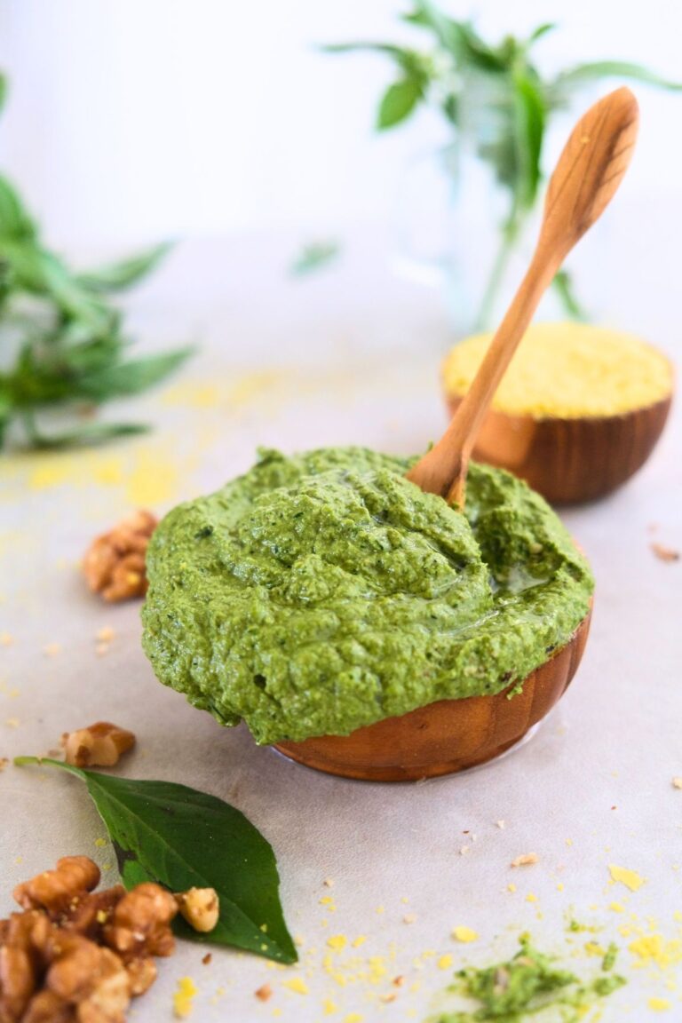 picture of walnut pesto in a wooden small bowl with walnuts, basil and nutritional yeast around it