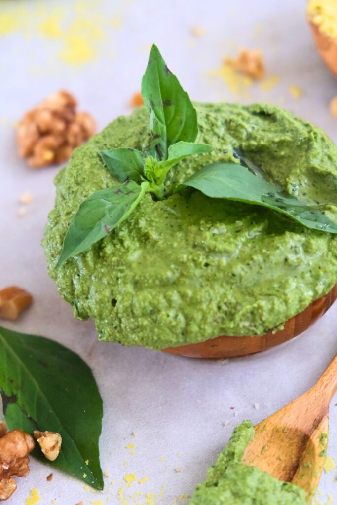 Walnut vegan basil pesto with large basil leaf on top in wood bowl