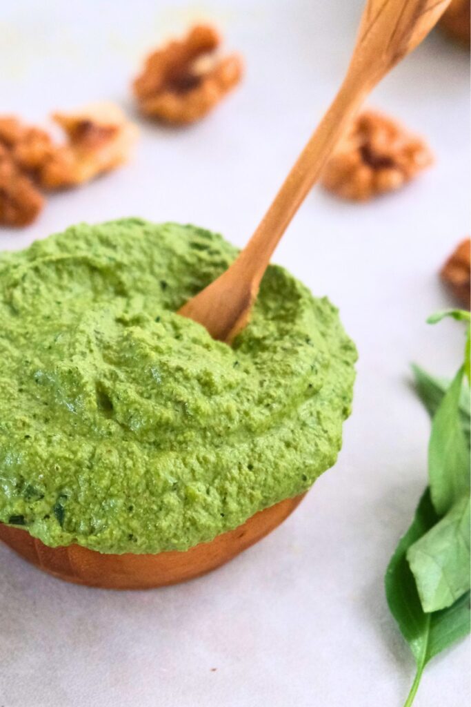 Walnut vegan basil pesto with small wood spoon in it. 