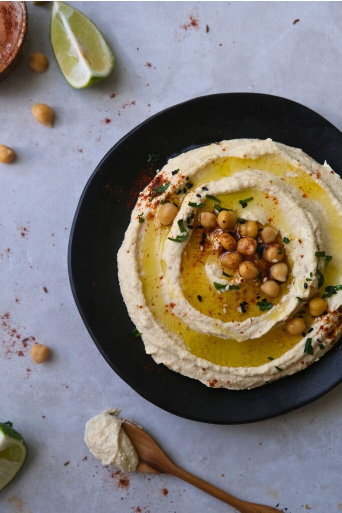 creamy hummus on a black plate with a drizzle of olive oil garnished with roasted chickpeas and parsley.