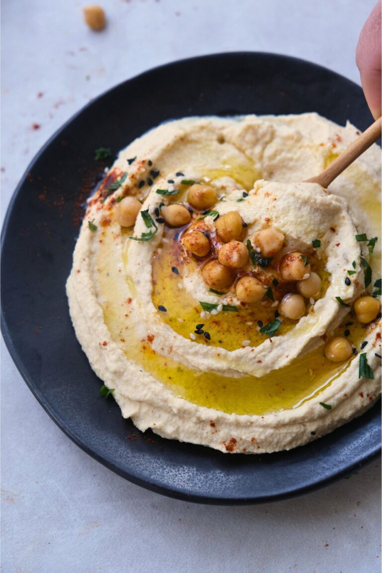 creamy hummus on a black plate with a drizzle of olive oil garnished with roasted chickpeas and parsley. Squeezing lime over the top.