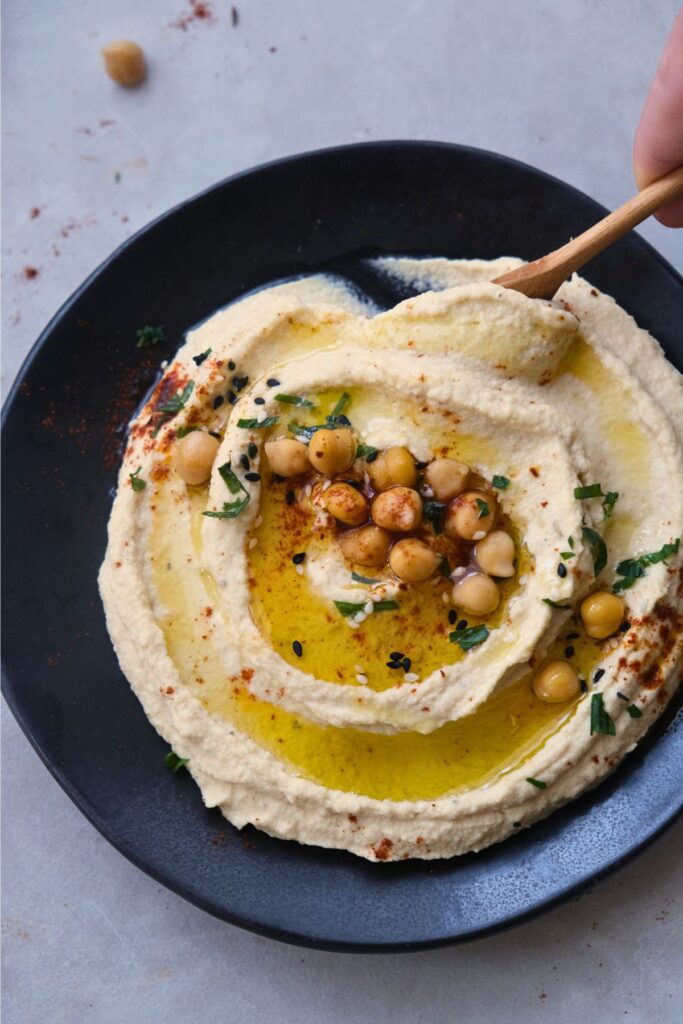 creamy hummus on a black plate with a drizzle of olive oil garnished with roasted chickpeas and parsley